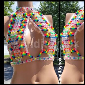 May include: A halter-style top constructed from clear plastic beads and vibrant multi-colored beads arranged in a geometric pattern. The garment features a high neck collar, an open chest design, and a beaded band that secures around the torso.