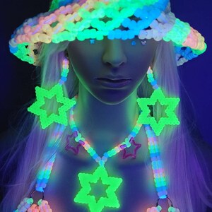 May include: A brightly glowing rave outfit, featuring a beaded hat, earrings, and a necklace with star pendants. The accessories glow against a dark backdrop, creating a vibrant, eye-catching look. The outfit is made of colourful beads.