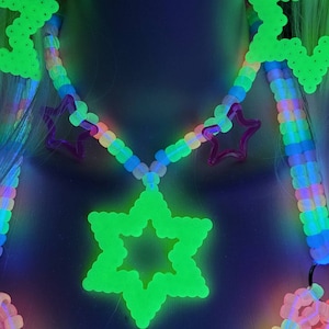 May include: A neon green star pendant necklace with a rainbow beaded chain and pink star accents. The necklace glows brightly against a dark background. The design includes a large star pendant and smaller star shapes.