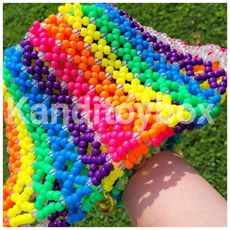 Peut inclure: Un accessoire en perles aux couleurs de l'arc-en-ciel avec le texte "Kanditoybox" en blanc. L'accessoire est compos&eacute; de petites perles color&eacute;es dans une vari&eacute;t&eacute; de couleurs, dont le rouge, l'orange, le jaune, le vert, le bleu et le violet. Les perles sont dispos&eacute;es en grille.