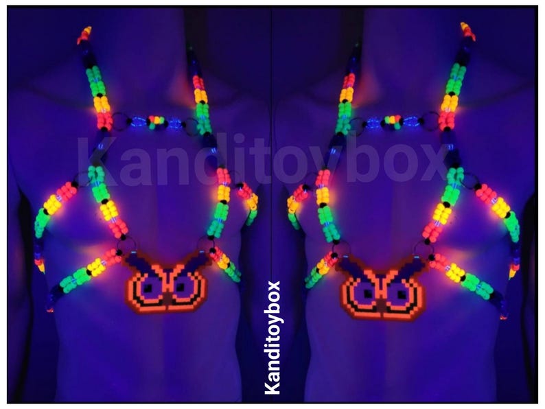 Peut inclure: Un harnais de corps en perles aux couleurs n&eacute;on avec un pendentif hibou pix&eacute;lis&eacute;. Le harnais est compos&eacute; de perles en plastique vert, jaune et orange vif reli&eacute;es par des anneaux m&eacute;talliques, brillant sous lumi&egrave;re UV avec le texte Kanditoybox.