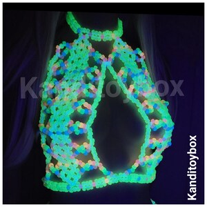May include: A halter-style top constructed from interconnected neon green, blue, and pink plastic beads that glow in the dark. The garment features a lattice pattern with a central cutout and the text Kanditoybox visible on the image.