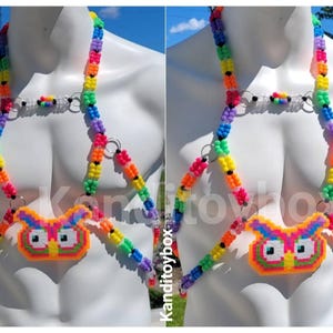 Peut inclure: Un harnais de corps compos&eacute; de perles en plastique multicolores vives dispos&eacute;es selon un motif g&eacute;om&eacute;trique. Le design pr&eacute;sente un pendentif central en forme de hibou fait de perles fusionn&eacute;es, reli&eacute; par des anneaux m&eacute;talliques argent&eacute;s.