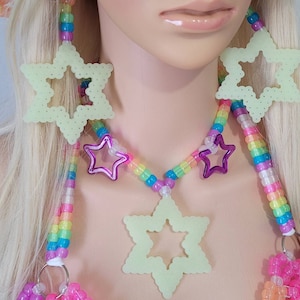 May include: A neon green star-shaped necklace and earrings set with a rainbow beaded chain. The necklace features a large star pendant and smaller purple star accents. The earrings are also star-shaped. The set is made of plastic beads.