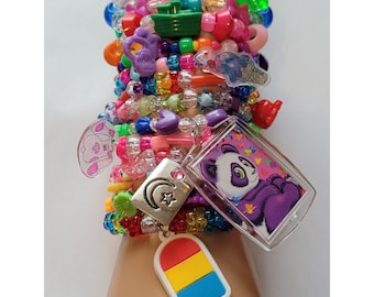May include: A collection of colorful beaded bracelets and charms. The bracelets feature various beads in shades of pink, blue, green, and yellow. Charms include a panda, a popsicle, and a crescent moon with a star.