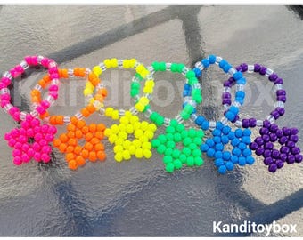 May include: Six circular bracelets arranged in a row, each featuring a five-pointed star charm made of plastic beads. The colors include pink, orange, yellow, green, blue, and purple. Each bracelet incorporates clear beads. The text Kanditoybox is visible.