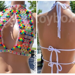 May include: A halter-style top constructed from clear and multi-colored rainbow plastic beads. The garment features a high neck, a cutout front design, and white fabric ties at the neck and back. The word Kanditoybox is visible on the image.