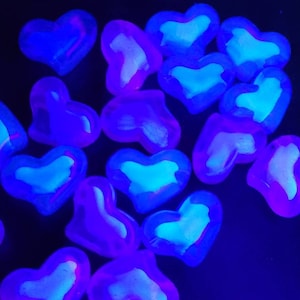 K&ouml;nnte beinhalten: Eine Ansammlung herzf&ouml;rmiger Objekte, die in einem Neonblau und Lila leuchten. Die Herzen haben eine hellere, fast wei&szlig;e Mitte, die einen auff&auml;lligen Kontrast zum dunklen Hintergrund bildet. Der Gesamteffekt ist ein lebendiges, auff&auml;lliges Display.