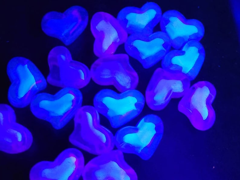 K&ouml;nnte beinhalten: Eine Ansammlung herzf&ouml;rmiger Objekte, die in einem Neonblau und Lila leuchten. Die Herzen haben eine hellere, fast wei&szlig;e Mitte, die einen auff&auml;lligen Kontrast zum dunklen Hintergrund bildet. Der Gesamteffekt ist ein lebendiges, auff&auml;lliges Display.