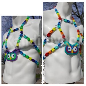 Peut inclure: Un harnais de corps compos&eacute; de perles en plastique multicolores dans des tons bleu, vert, jaune, orange, rouge et blanc, reli&eacute;es par des anneaux en m&eacute;tal argent&eacute;. Le design pr&eacute;sente un pendentif hibou pix&eacute;lis&eacute; en violet, vert et bleu.