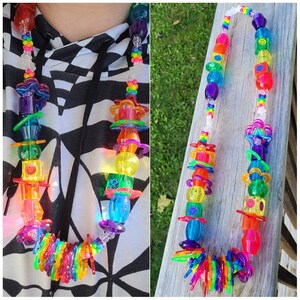 May include: A colorful necklace featuring a variety of transparent plastic beads in rainbow hues. The necklace includes smiley face beads, star-shaped elements, and other geometric shapes. The design is vibrant and playful, suitable for a fun, eye-catching accessory.