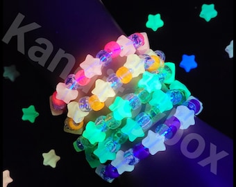 May include: Several colorful beaded bracelets with star-shaped beads. The bracelets are arranged in a stack, with each bracelet featuring a different color scheme. The star beads glow in the dark, creating a vibrant effect. The background is dark.