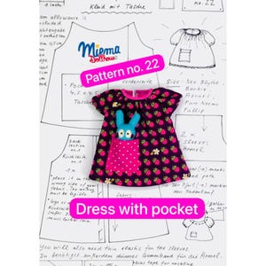 May include: A dark purple doll dress with a repeating raspberry pattern, featuring a bright pink pocket with white polka dots. A small blue felt rabbit figure is tucked inside the pocket. The dress is displayed over a sewing pattern sheet labeled Pattern no. 22 and Dress with pocket.