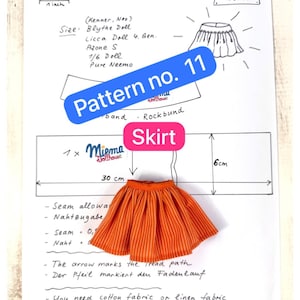 May include: A sewing pattern sheet for a doll skirt labeled Pattern no. 11, featuring a hand-drawn diagram with measurements of 30 cm by 6 cm, and a physical orange skirt with thin white vertical stripes placed over the printed instructions.
