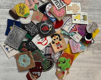 May include: A collection of colorful felt patches with various designs and sayings, including "Just Peachy", "Mess Express", "Hearsa Objection", "Go Better On You", and "Kindashady".