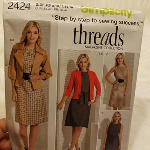 Op de afbeelding: Een naaipatroonpakket voor een jurk met drie verschillende stijlen. Het pakket is van de Simplicity Threads Magazine Collection en bevat de maten K5 8, 10, 12, 14, 16, EUR. 34-42, FR. 36-44. Het patroon is voor een jurk met een getailleerd bovenstuk en een rok die tot op de knie valt. De eerste stijl heeft een bruin en wit gebloemde jurk met een bruin jasje. De tweede stijl heeft een grijze jurk met een rood jasje. De derde stijl heeft een zwarte jurk met een zwarte band.