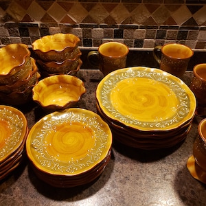 May include: A set of brown and green ceramic dinnerware with a swirl pattern. The set includes plates, bowls, and mugs.