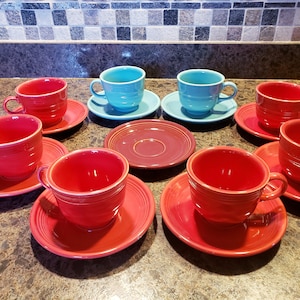 May include: A set of eight ceramic teacups and saucers. Six of the cups and saucers are red, and two are a light blue color.