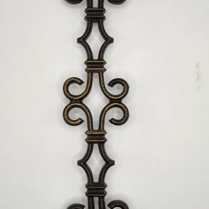Könnte beinhalten: Verziertes, dunkelbronze-farbenes dekoratives Metallelement mit Scroll- und rautenförmigen Designs. Das symmetrische Stück weist ein sich wiederholendes Muster aus geschwungenen und eckigen Formen auf, geeignet für Heimdekoration oder architektonische Akzente.