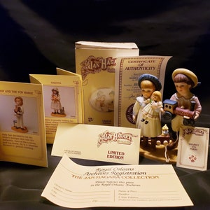 Könnte beinhalten: Eine Porzellanfigur-Set mit zwei Kindern, einem Jungen und einem Mädchen, mit einem Spielzeugzug und einer Puppe. Der Junge trägt ein blaues Hemd, einen Strohhut und eine braune Hose. Das Mädchen trägt ein weißes Kleid mit einer blauen Schärpe. Die Figur ist Teil der Royal Orleans Archives Registration, The Jan Hagara Collection.