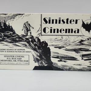May include: A rectangular white box with black ink illustrations featuring a couple standing on a cliff, a car, and flying saucers. The text reads Sinister Cinema, The leading source of horror, mystery & science-fiction on video, and address details.