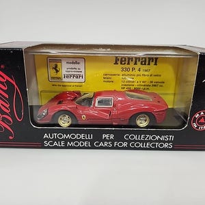 May include: A 1:43 scale red Ferrari 330 P.4 1967 model car inside a black Bang brand display box. The box features yellow interior backing with technical specifications and the Ferrari logo. The car has gold wheels and a low-profile body design.