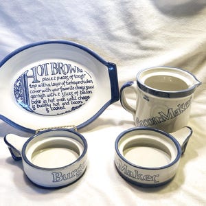 Puede incluir: Un juego de fuentes de cerámica blanca con ribete azul. La fuente ovalada tiene el texto "HOT BROWN" y una receta. Hay una taza que dice "Bacon Maker" y dos platos pequeños que dicen "Burger Maker".