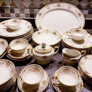 May include: A set of vintage fine china dinnerware with a floral pattern in shades of blue, pink, and gold. The set includes plates, bowls, cups, and saucers.