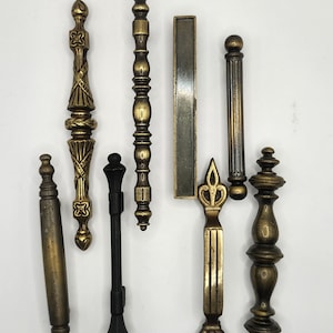 May include: A collection of antique cabinet pulls and handles in various shapes and sizes. The hardware features ornate designs and a range of finishes, including brass and black. The pulls are likely for furniture restoration or decorative projects.