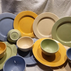 May include: A collection of colorful ceramic bowls and plates in shades of blue, yellow, green, and cream. The bowls and plates are arranged in a random pattern on a white surface.