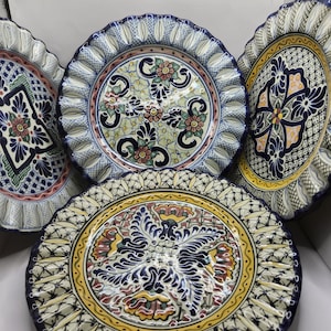 May include: A collection of decorative ceramic plates with intricate floral and geometric designs. The plates feature a scalloped edge and a vibrant color palette including blue, yellow, red, and green. The plates are likely for decorative use.