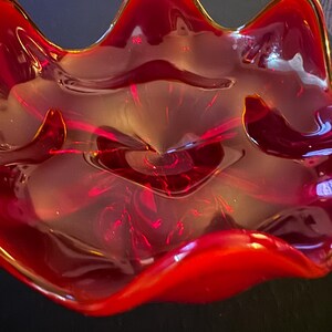 May include: A vibrant, ruby-red glass bowl with a wavy, organic shape. The bowl's edges are gently curved, and the glass has a glossy finish. The bowl is likely used for decorative purposes or serving.