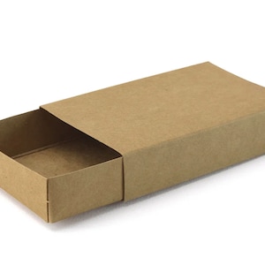 May include: A rectangular, open cardboard box in a natural kraft paper colour with a sliding lid. The box is partially open, showing the inside. The box is on a white surface.