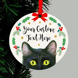 May include: A round Christmas ornament featuring a black cat peeking out from behind a green holly wreath with red berries. The ornament has a white background with gold stars and the text "Your Custom Text Here".