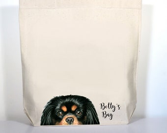 May include: A white canvas tote bag with black handles. The bag has a black and brown Cavalier King Charles Spaniel peeking out from the bottom and the text "Betty's Bag" printed on the bottom right corner.