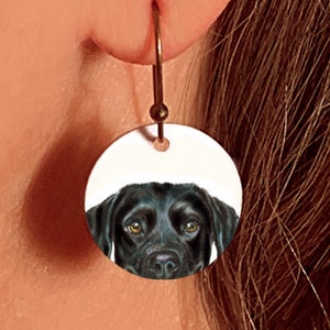 May include: Black Labrador Retriever dog face on a round white ceramic earring.