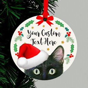 May include: Round Christmas ornament featuring a black cat wearing a red Santa hat peeking out from behind a green holly wreath with red berries and gold stars. The text "Your Custom Text Here" is written in black on the ornament.
