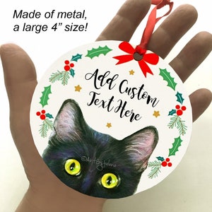 May include: A black cat with green eyes peeks out from behind a white, round Christmas ornament. The ornament is decorated with a red bow, holly leaves, and red berries. The text "Add Custom Text Here" is printed on the ornament. The ornament is made of metal and measures 4 inches in diameter.