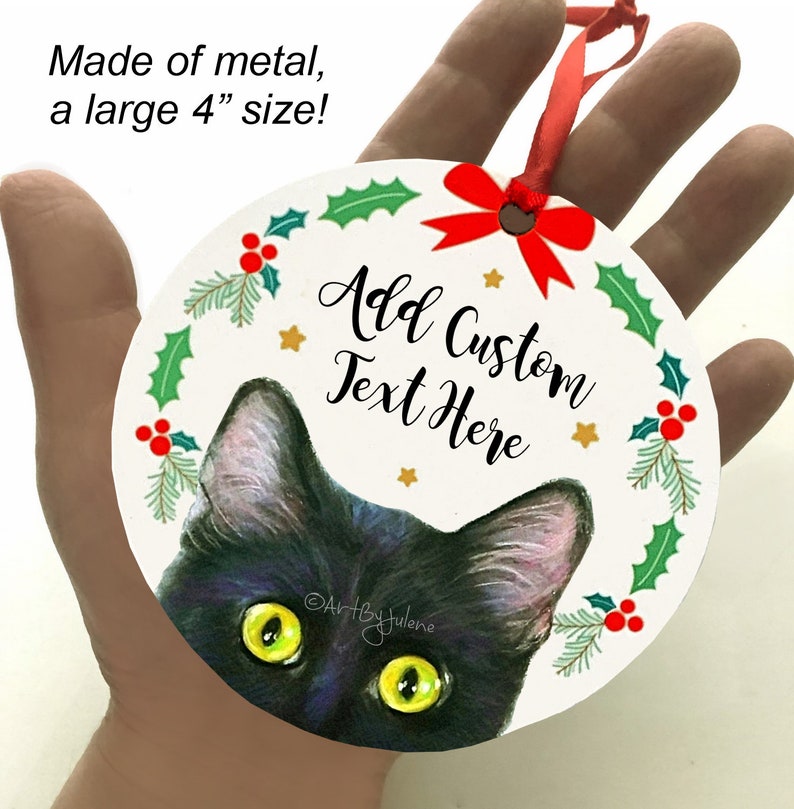 May include: A black cat with green eyes peeks out from behind a white, round Christmas ornament. The ornament is decorated with a red bow, holly leaves, and red berries. The text "Add Custom Text Here" is printed on the ornament. The ornament is made of metal and measures 4 inches in diameter.