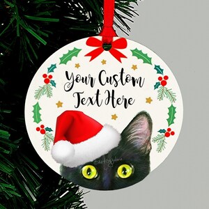 May include: Round Christmas ornament featuring a black cat wearing a red Santa hat peeking out from behind a green holly wreath. The ornament has the text "Your Custom Text Here" in black.