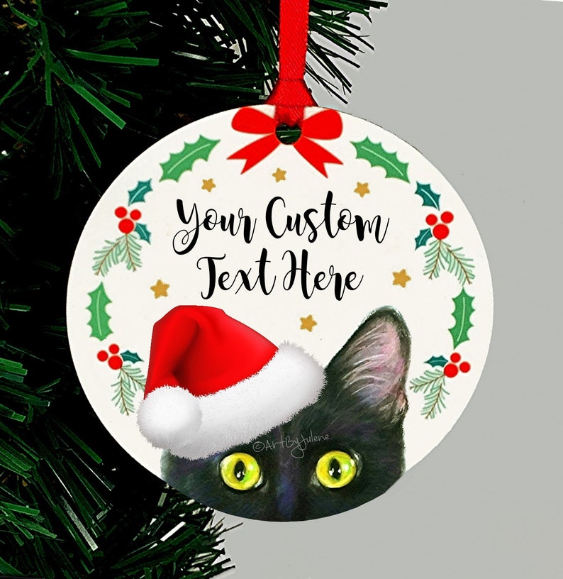 May include: Round Christmas ornament featuring a black cat wearing a red Santa hat peeking out from behind a green holly wreath. The ornament has the text "Your Custom Text Here" in black.