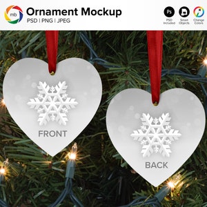 May include: Two white heart-shaped Christmas ornaments with a snowflake design hanging on a Christmas tree with white lights. The ornaments have the words "FRONT" and "BACK" printed on them.