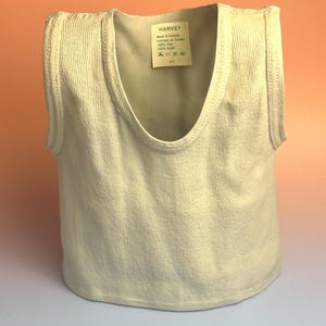 May include: A white ceramic sculpture shaped like a sleeveless tank top with a ribbed texture. A label inside the neckline reads HARVEY, Made in Canada, Fabriqué au Canada, 100% Clay, 100% Argile, with care symbols and the size S/P printed below.