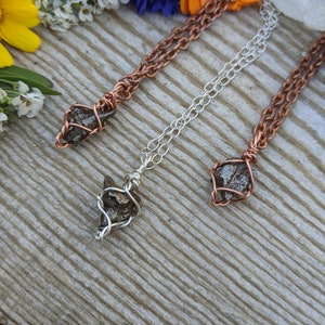 Puede incluir: Tres collares con colgantes de cristal en bruto envueltos en alambre. Los collares est&aacute;n hechos de alambre de cobre, plata y cobre. Los cristales son de color marr&oacute;n oscuro y tienen una textura rugosa y natural.