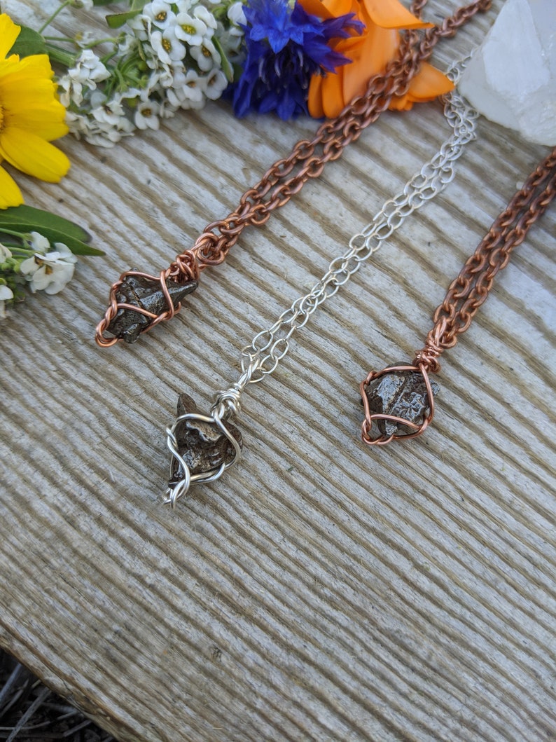 Puede incluir: Tres collares con colgantes de cristal en bruto envueltos en alambre. Los collares est&aacute;n hechos de alambre de cobre, plata y cobre. Los cristales son de color marr&oacute;n oscuro y tienen una textura rugosa y natural.