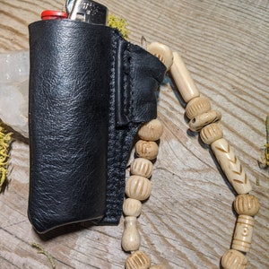Puede incluir: Una funda de cuero negro para encendedor con una correa de cuentas. Las cuentas est&aacute;n hechas de hueso natural y tienen tallas intrincadas.