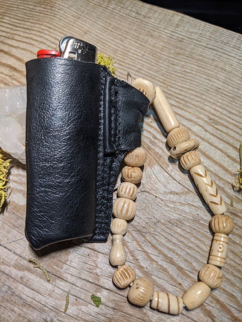 Puede incluir: Una funda de cuero negro para encendedor con una correa de cuentas. Las cuentas est&aacute;n hechas de hueso natural y tienen tallas intrincadas.
