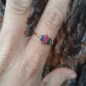 Peut inclure: Une délicate bague en fil de fer enroulé autour de trois petites pierres précieuses. Les pierres précieuses sont de couleur rouge foncé, bleu foncé et verte.