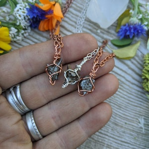 Puede incluir: Tres colgantes de alambre envueltos en cobre y plata con peque&ntilde;as piedras naturales rugosas de color gris oscuro. Los colgantes cuelgan de cadenas.