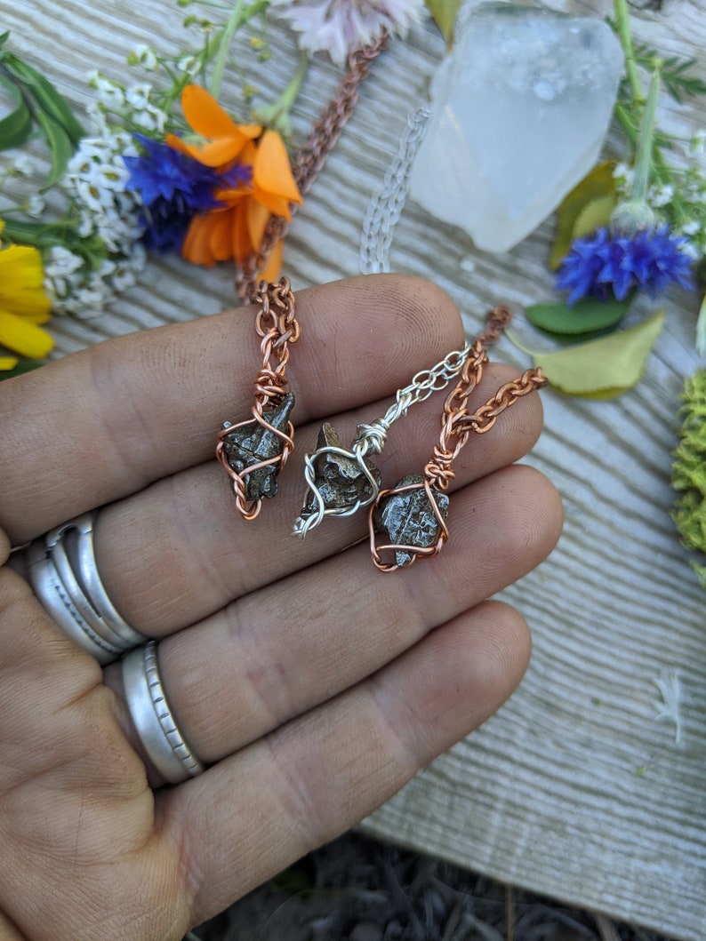 Puede incluir: Tres colgantes de alambre envueltos en cobre y plata con peque&ntilde;as piedras naturales rugosas de color gris oscuro. Los colgantes cuelgan de cadenas.